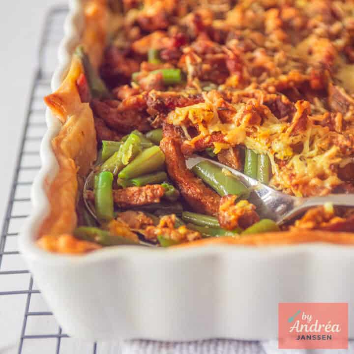 A square photo showing part of a white baking dish with puff pastry, green beans, cheese and shawarma meat.