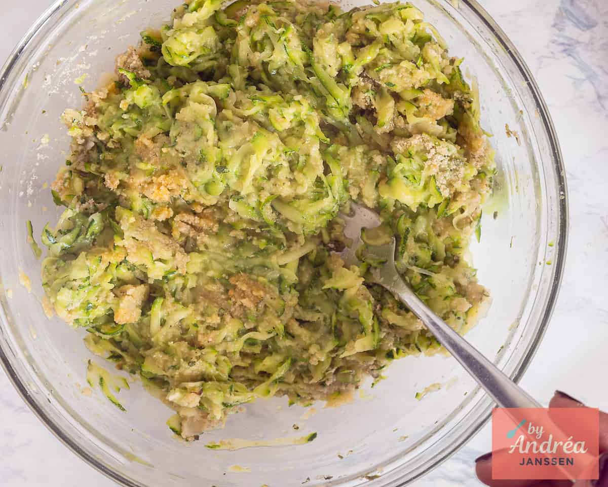 Meng courgette, paneermeel en smaakmakers door elkaar in een glazen schaal.