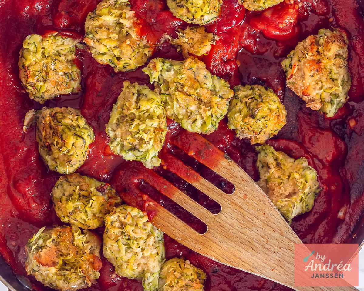 Gegaarde courgette balletjes worden toegevoegd aan de tomatensaus