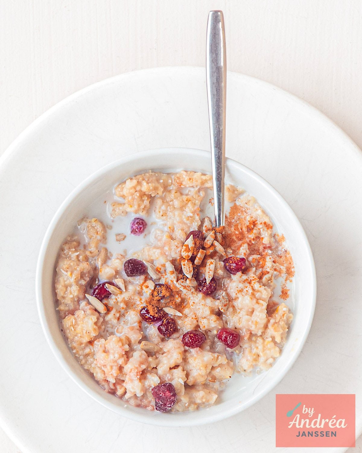 Een wit bord met een witte kom met havermout granaatappel en zonnebloempitten