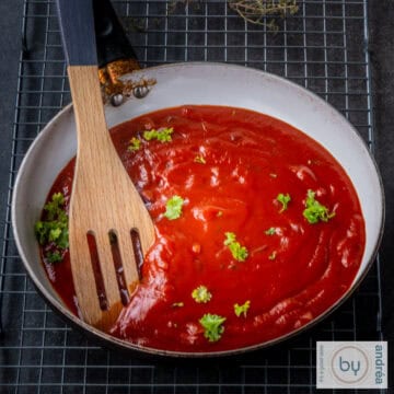 A square picture with a skillet filled with enchilada sauce. A wooden spoon in the skillet.