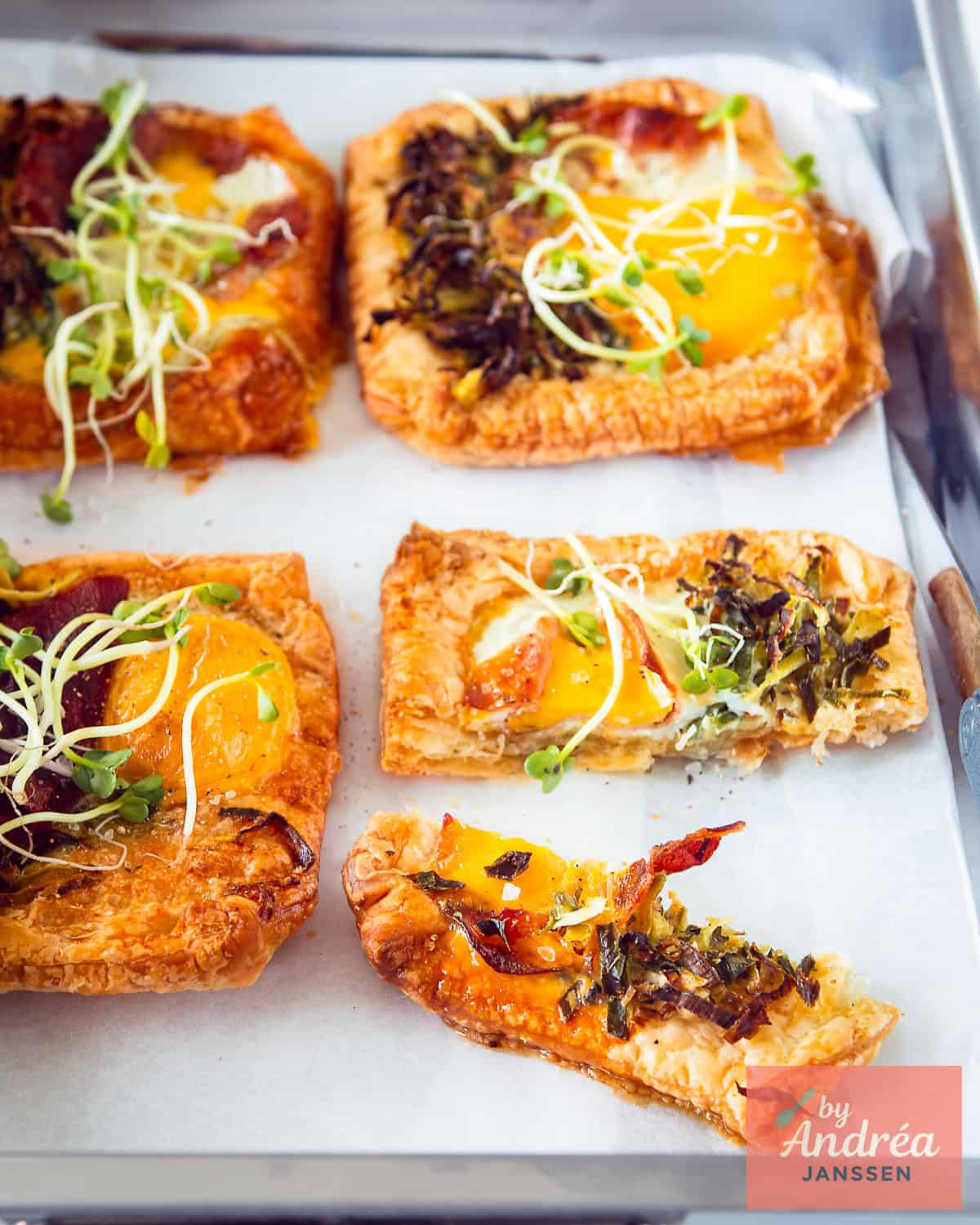 A baking dish with four puff pastry cups topped with egg, leek, and bacon. Cut in half at the bottom right.