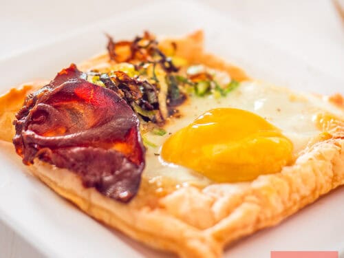 A square photo of a puff pastry cup filled with egg, bacon and fried leek