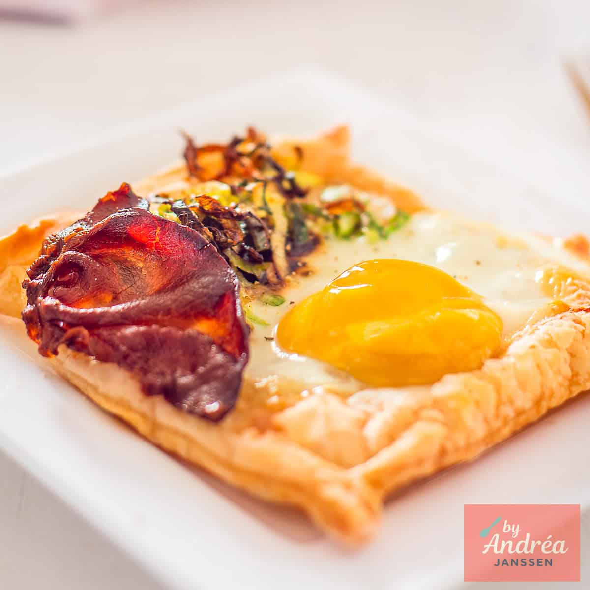 A square photo of a puff pastry cup filled with egg, bacon and fried leek