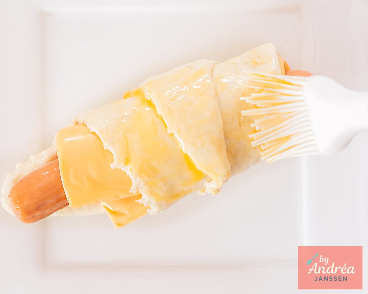 Give an egg wash to a pig in a blanket on a white plate