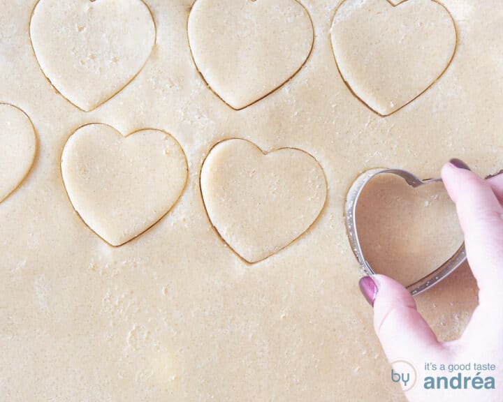 Cookies are cut out of the dough with a heart cutter.