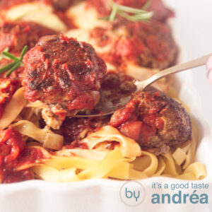 A square photo of a white casserole dish filled with tagliatelle, meatballs and homemade tomato sauce