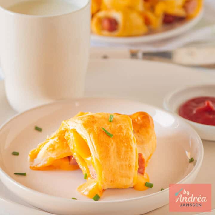 A square picture of a white plate with a cheesy pig in a blanket on top.