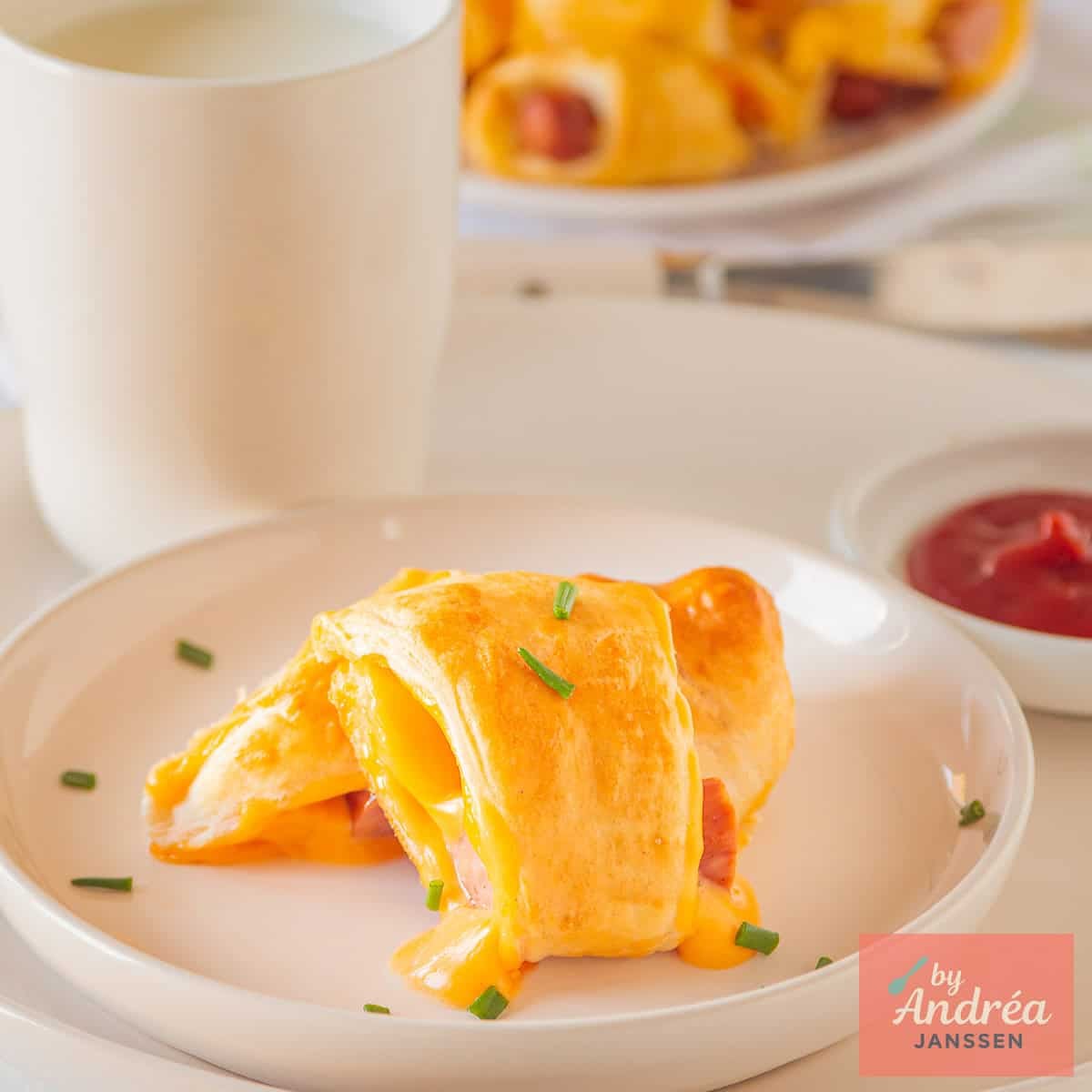 A square picture of a white plate with a cheesy pig in a blanket on top.