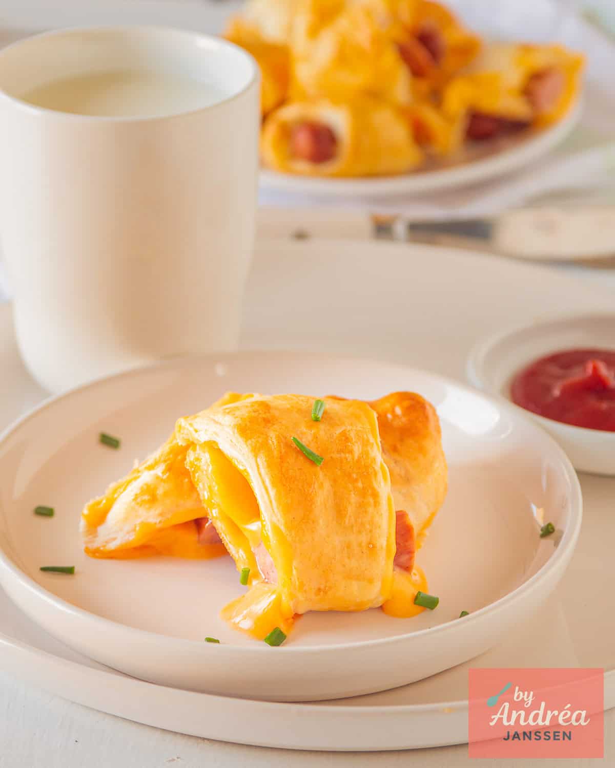 A white plate with a cheesy frankfurter puff pastry pig in a blanket. Some more in the background