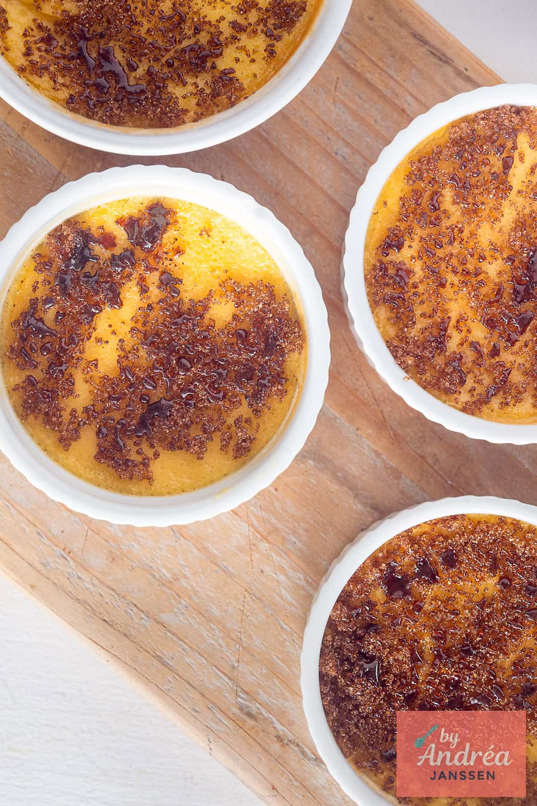A top down picture with a wooden board with ramekins with cream brulee pudding with cinnamon and honey