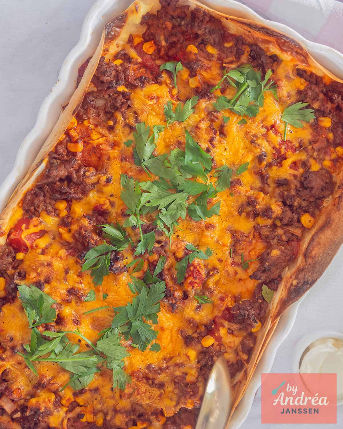 Een foto van bovenaf van een ovenschaal met tortilla, gehakt en kaas in een romige tomatensaus.