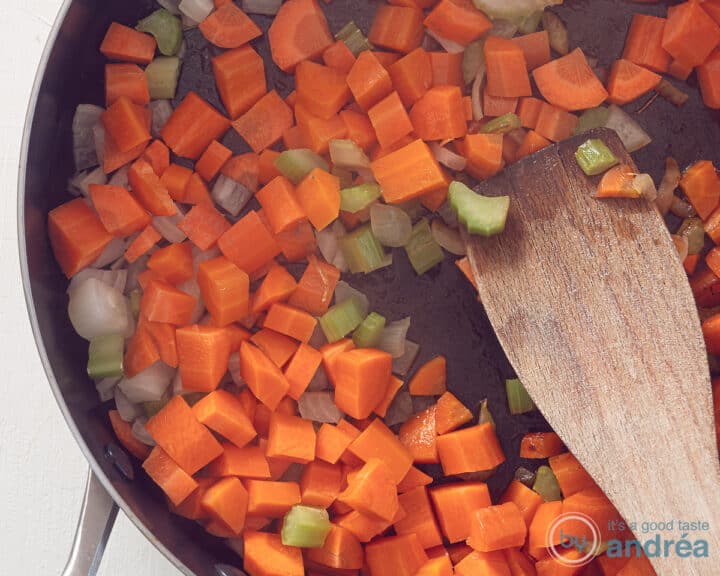 A pan in which onion, carrot and celery are fried. A wooden spatula is inside.