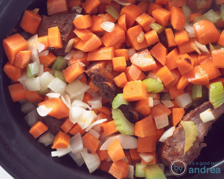 A slow cooker filled with ribs, carrot, celery and onion cubes.