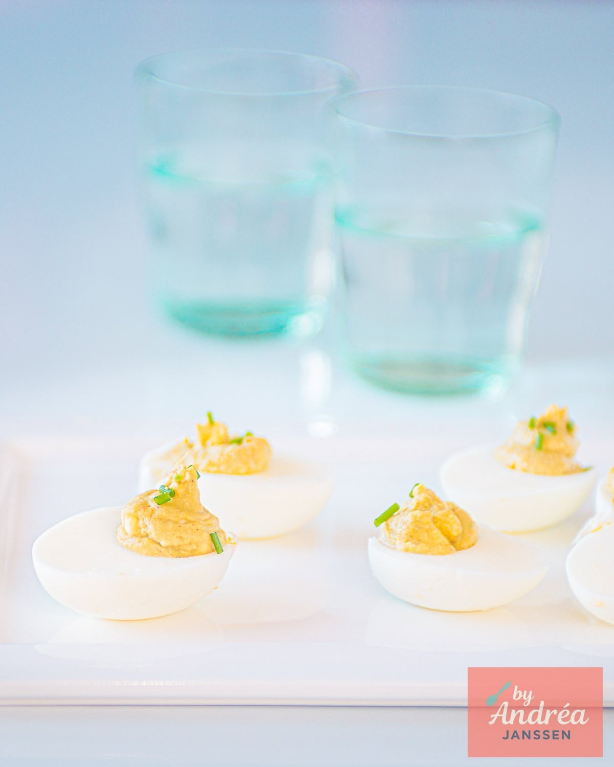 A bowl of avocado-deviled eggs, two blue glasses in the back