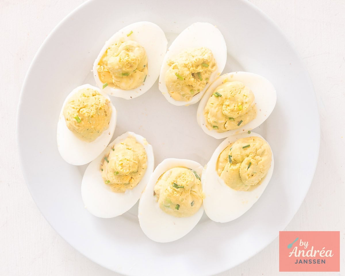 A white plate with avocado deviled eggs sprinkled with chives in a round form