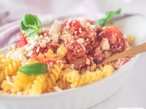A square photo with a white oven dish with pasta with feta, tuna and tomato