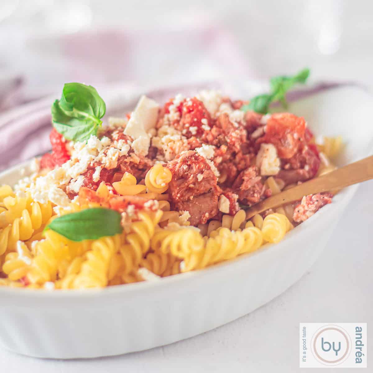 A square photo with a white oven dish with pasta with feta, tuna and tomato