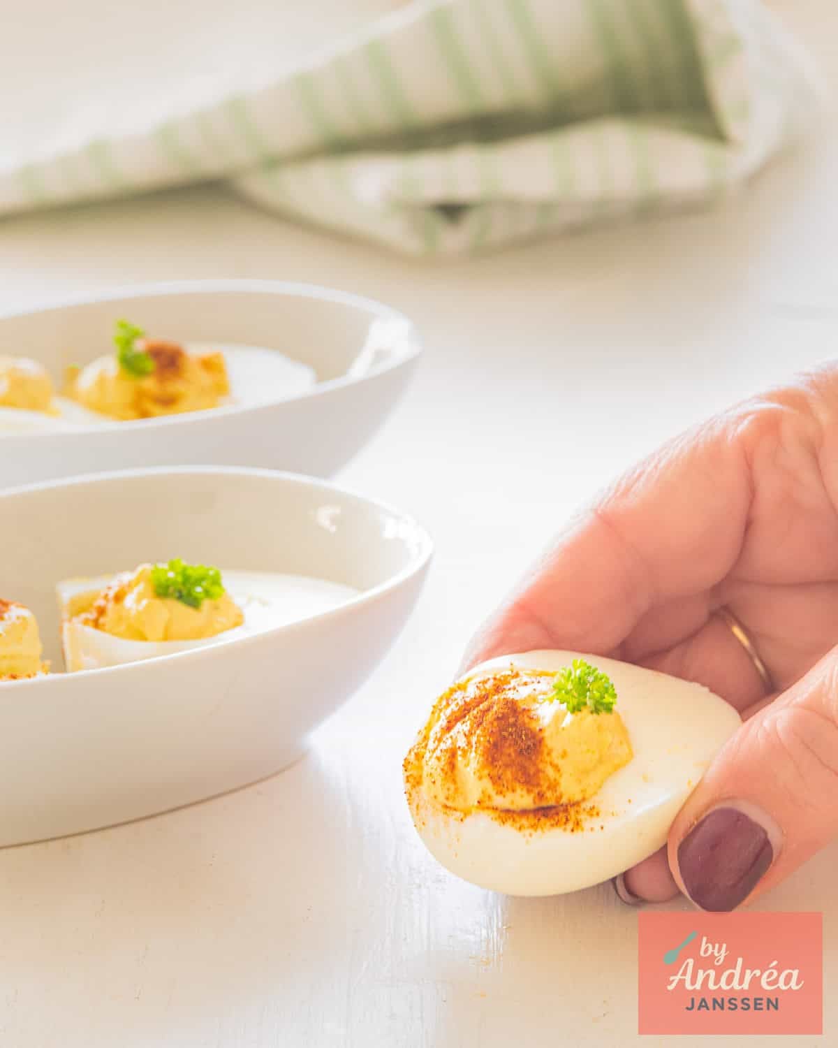 A hand holding a deviled egg with curried filling. Some more in bowls in the background