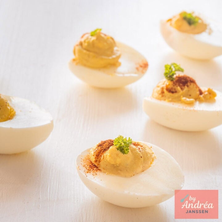 A square picture with deviled eggs with a filling of curry, Worcestershire and paprika on a white backdrop