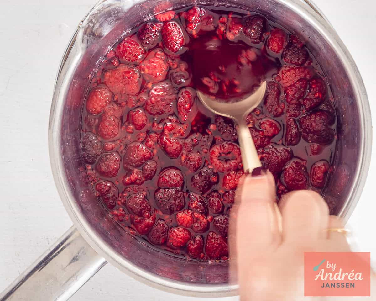 A pan of raspberries with a spoon squeezing out the juice.