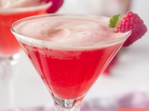 A square photo with a cocktail glass filled with raspberries, gin and Prosecco