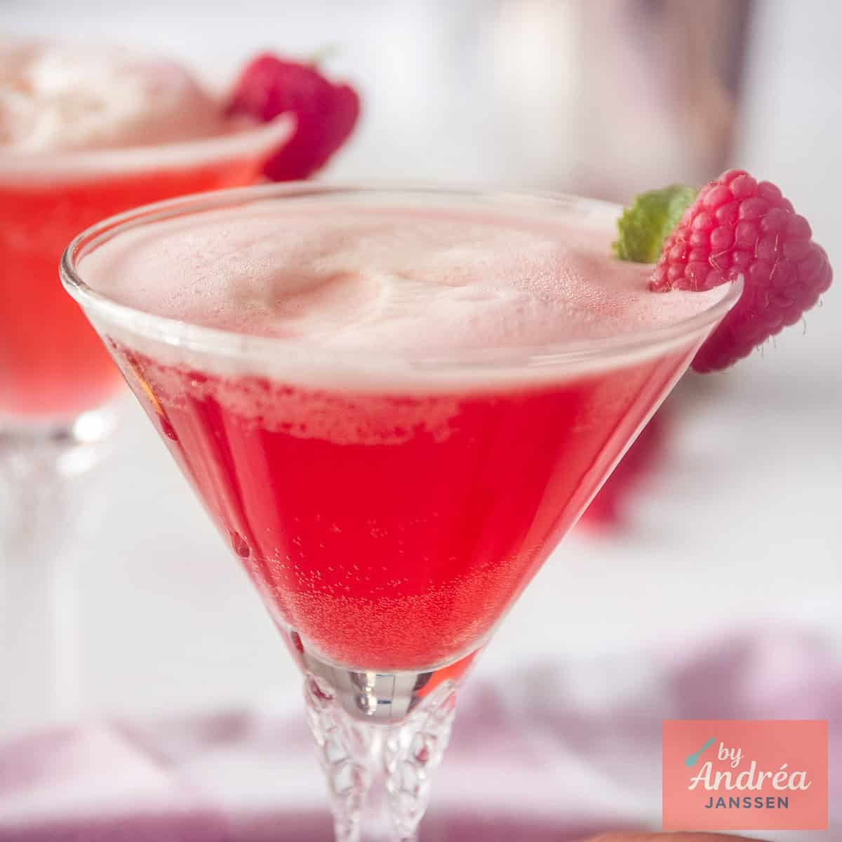 A square photo with a cocktail glass filled with raspberries, gin and Prosecco