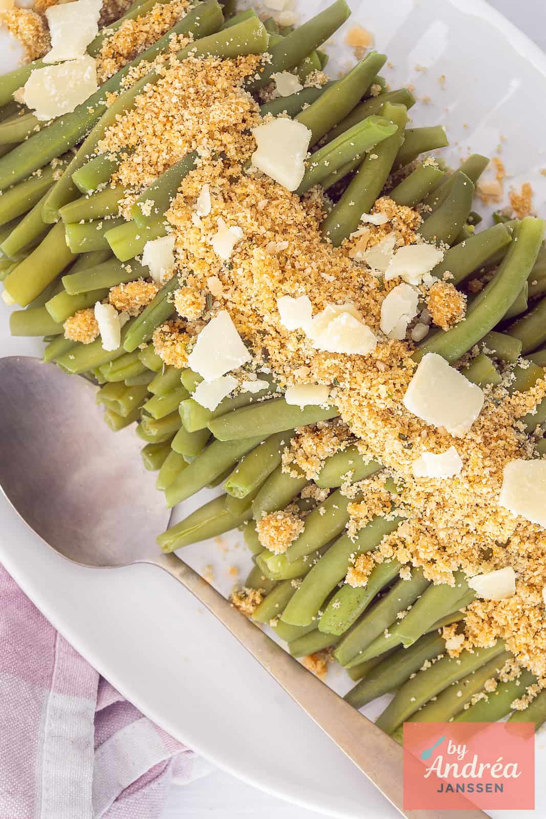 A top-down photo of a white platter with herb breadcrumbs, green beans, and Parmesan cheese.