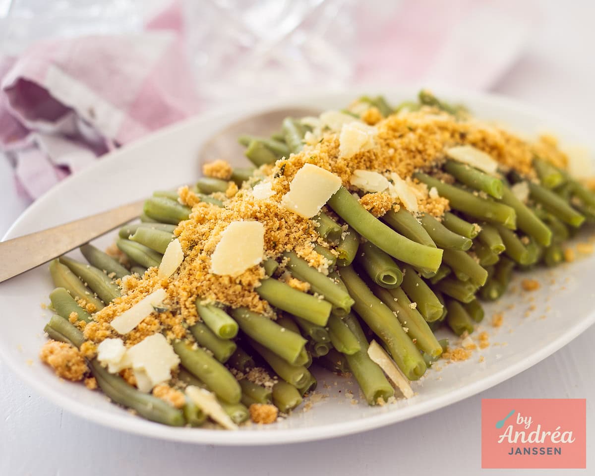 A wide shot of a white bowl of green beans with herb paneer and Parmesan cheese