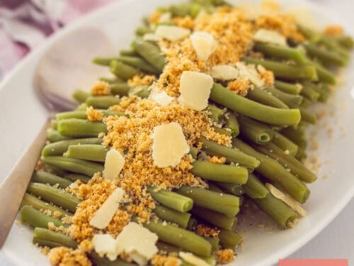 Roasted asparagus with Parmesan cheese and breadcrumbs on a white platter, garnished for a gourmet meal.