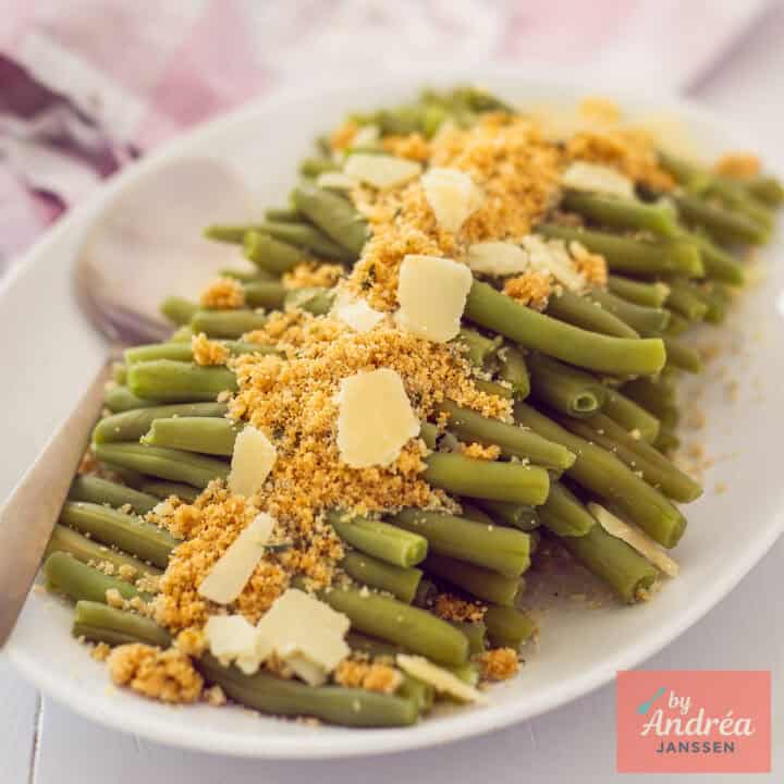 Roasted asparagus with Parmesan cheese and breadcrumbs on a white platter, garnished for a gourmet meal.