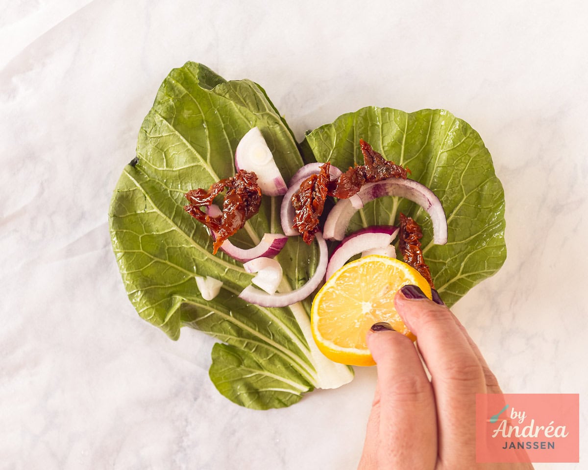 A baking sheet with a bed of bok choy, lemon, sun-dried tomatoes and red onion