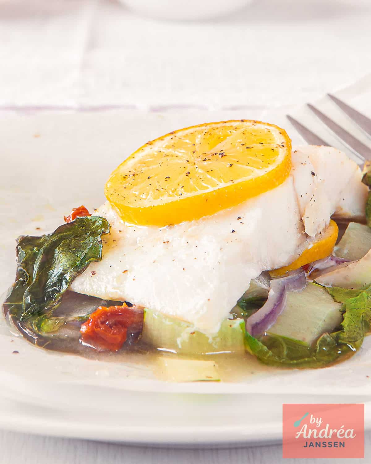 A white plate with steamed cod on a bed of bok choy and seasonings.