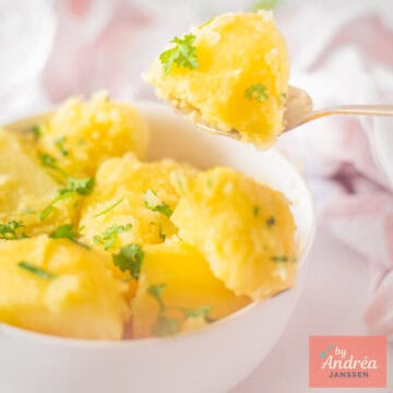 A square picture with a white bowl which a spoon takes some potatoes with parsley from