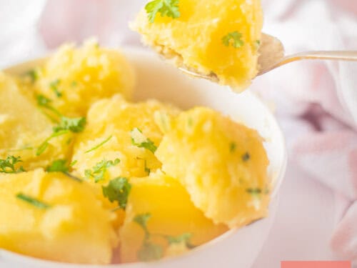 A square picture with a white bowl which a spoon takes some potatoes with parsley from