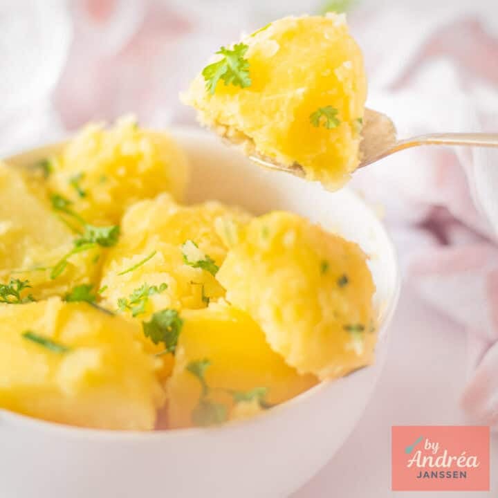 A square picture with a white bowl which a spoon takes some potatoes with parsley from