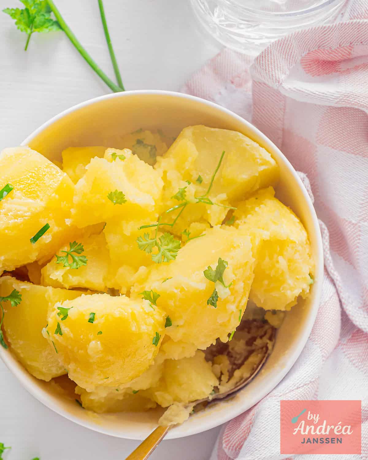 A picture from above from a white bowl with parsley potatoes cooked with some butter.