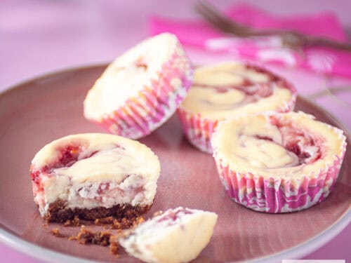 A square photo with a pink plate with pink cupcakes, four of which 1 is broken in half and you can clearly see the bottom.