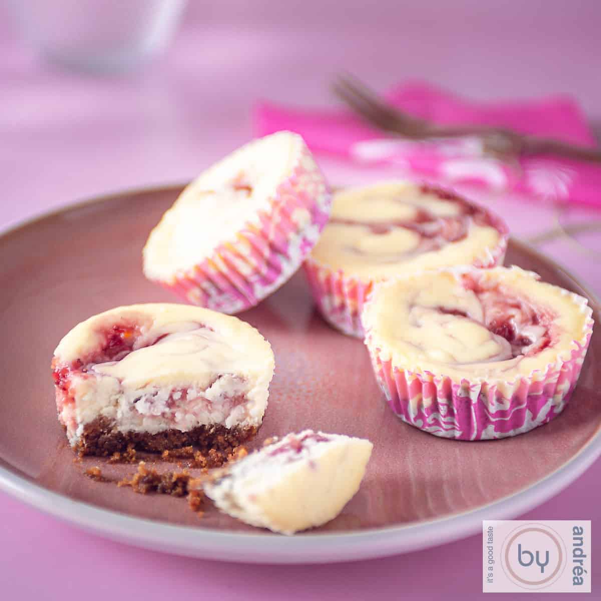 A square photo with a pink plate with pink cupcakes, four of which 1 is broken in half and you can clearly see the bottom.