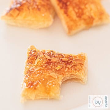 A square photo of lemon cookies with an almond layer. A bite has been taken from the front cookie.