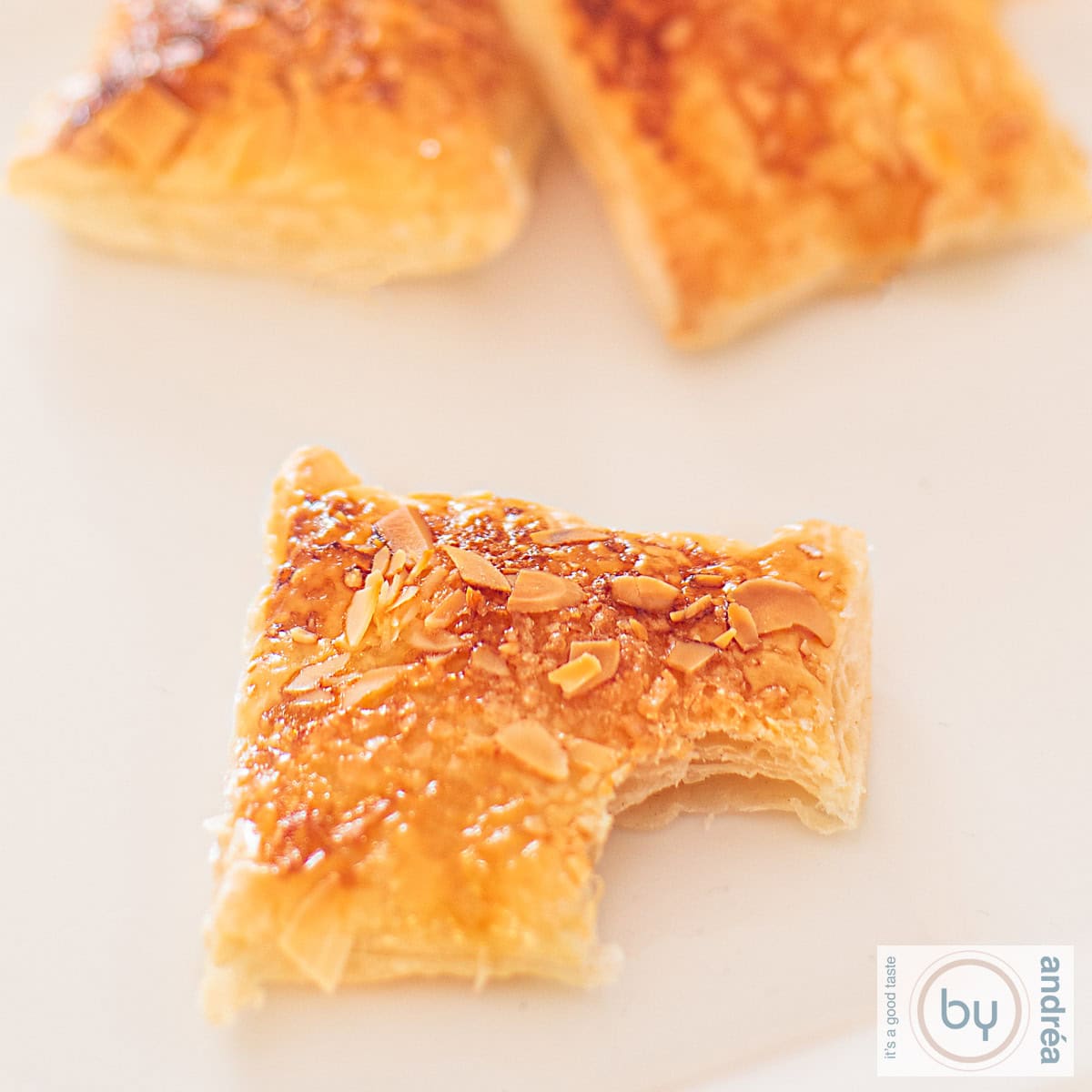 A square photo of lemon cookies with an almond layer. A bite has been taken from the front cookie.