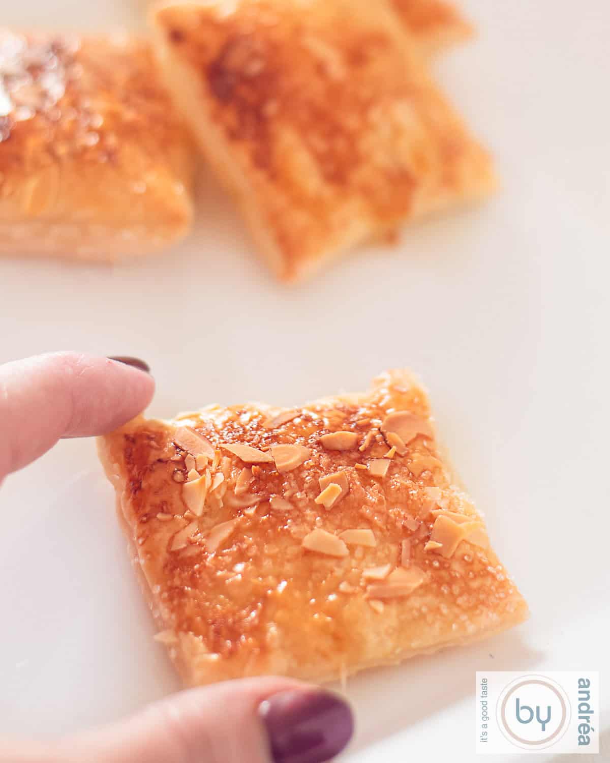 A height photo with a lemon puff pastry cookie with almond. A hand is holding the cookie.