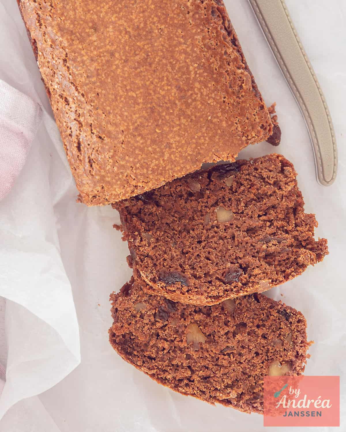A photo from above of a gingerbread with two cut slices containing nuts and currants.