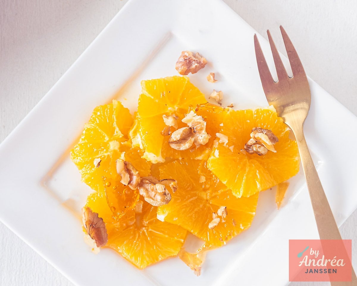 A plate with an orange dessert with honey marinade, caramel and walnuts