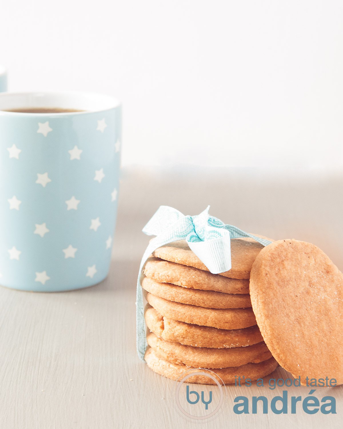 A grey underground with a stack of cookies with a blue ribbon. Two blue coffee cups in the left corner.