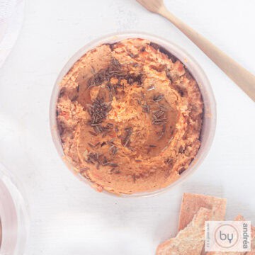 A square picture with a bowl filled with sweet potato and chickpea hummus. Some crackers laying aside