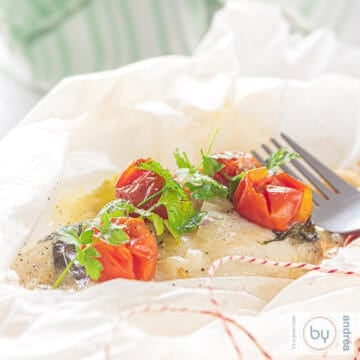 A square photo with an open baking paper filled with fried cod with cheese and vegetables