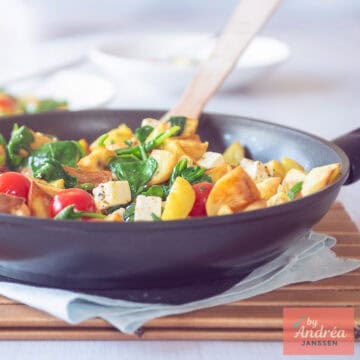 A square photo showing part of a wok filled with stir-fried potatoes, feta, spinach and tomato.