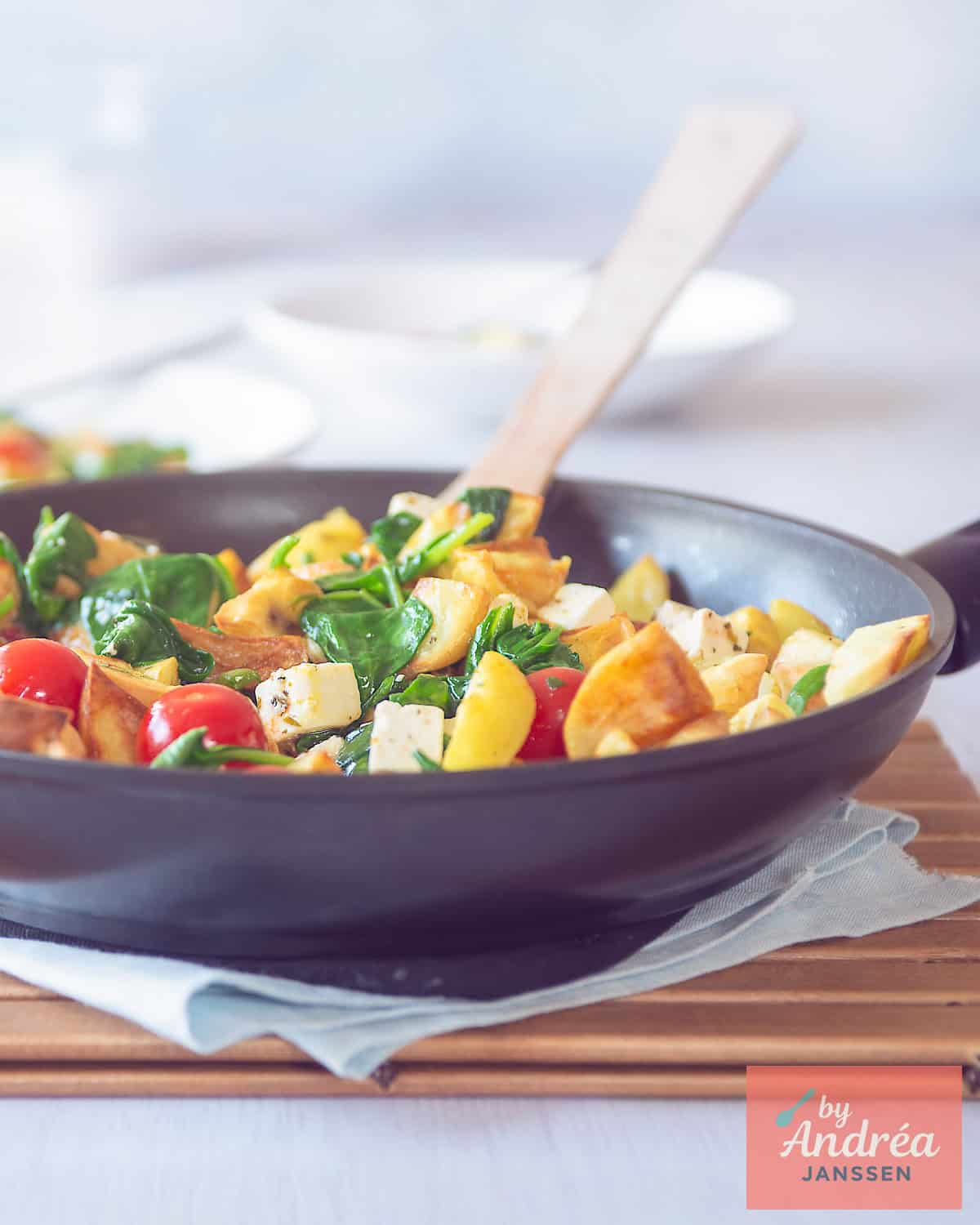 Een pan gevuld met gewokte aardappeltjes, feta, spinazie en tomaatjes