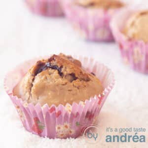 A square photo with in the foreground a muffin with chocolate and coconut, gluten-free and in the background three muffins (partly visible). The muffins are in grated coconut.
